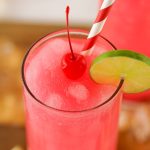 Bright pink slushy Dirty Shirley cocktail topped with a maraschino cherry and lime slice, served with a red and white striped straw in a tall glass.