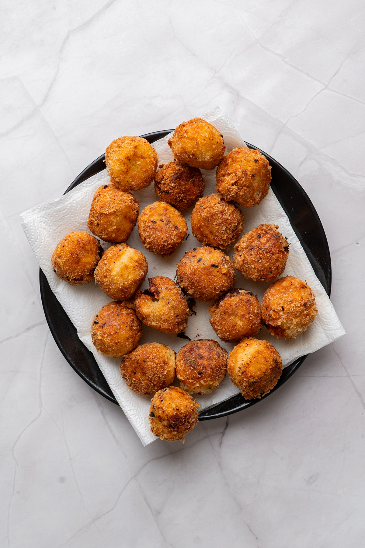 These fried mashed potato balls are crispy, golden, and loaded with cheesy flavor. The perfect way to turn leftover mashed potatoes into an irresistible side or snack. Freshly fried mashed potato balls resting on a paper towel-lined plate, showing their golden, crispy exterior after frying.