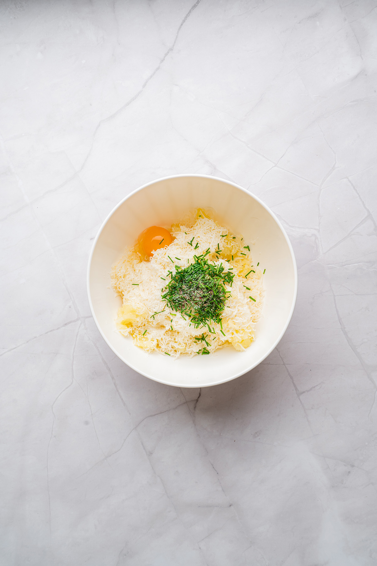 These fried mashed potato balls are crispy, golden, and loaded with cheesy flavor. The perfect way to turn leftover mashed potatoes into an irresistible side or snack. Mixing bowl filled with mashed potatoes, shredded cheese, chives, egg, and seasonings before being combined into a smooth mixture.