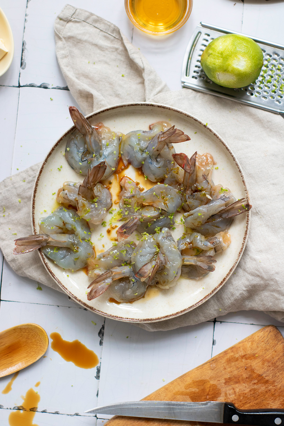 Garlic chili butter shrimp boats are quick, flavorful, and a little fancy. Juicy shrimp sit on vermicelli noodle nests that soak up every drop of the buttery garlic-chili sauce. Butterflied shrimp seasoned with lime zest and fish sauce on a plate, ready for shrimp boat assembly.
