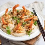 Overhead view of steamed shrimp boats on a white platter, nestled on rice vermicelli and drizzled with chili garlic sauce.