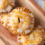 Golden apple hand pies with flaky crust and vanilla glaze drizzled on top, served on a wooden tray.