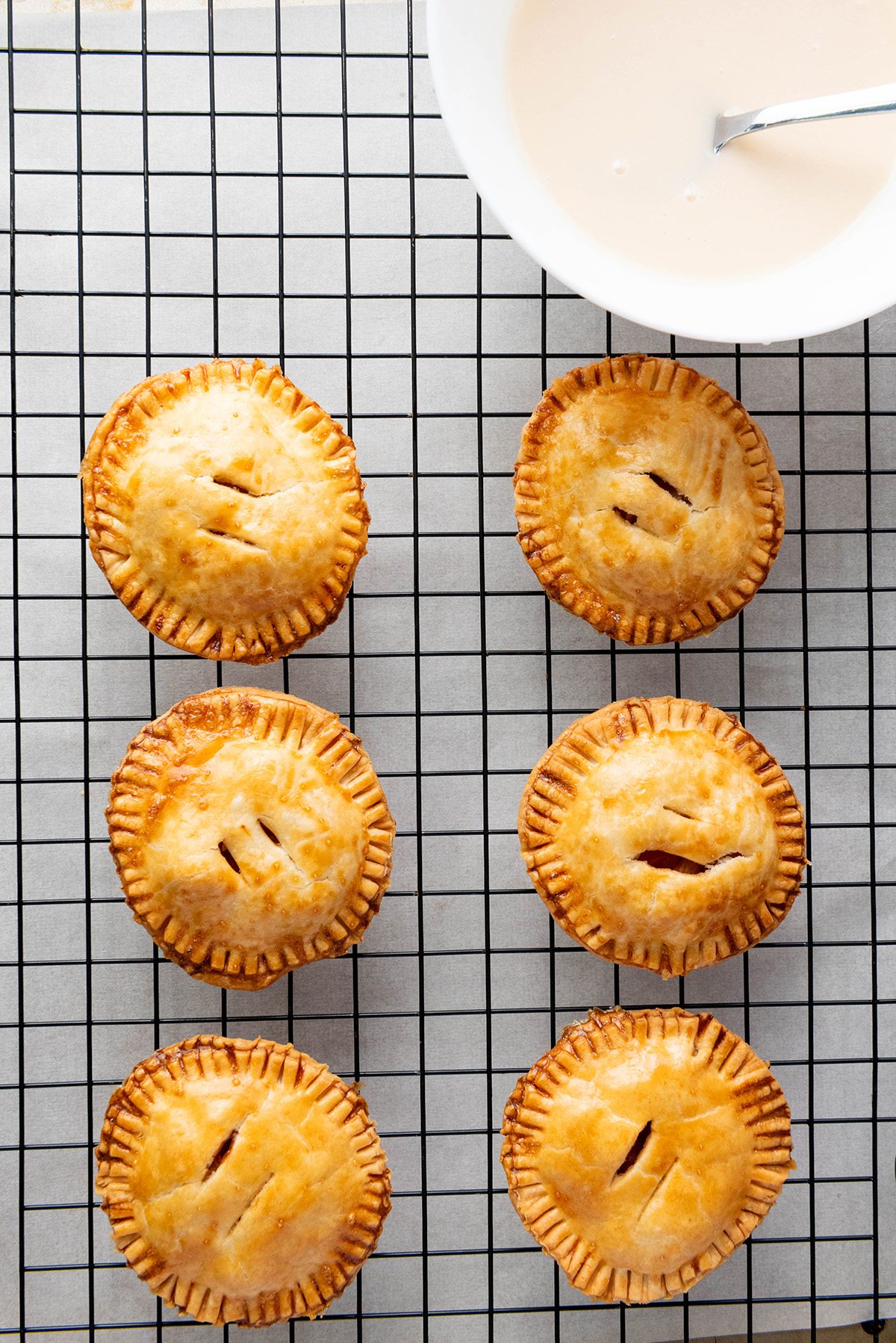 Cozy up with these easy apple hand pies made with flaky store-bought crust and a sweet cinnamon filling. All the comfort of homemade apple pie in an easy grab-and-go treat. Freshly baked apple hand pies cooling on a wire rack before adding glaze.