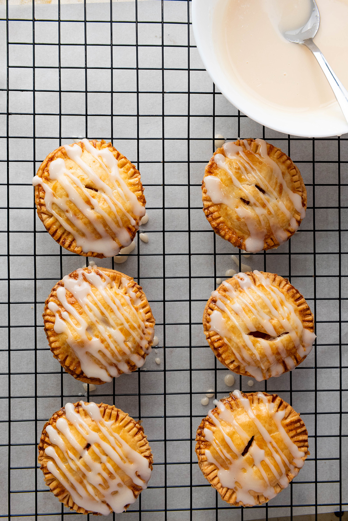 Cozy up with these easy apple hand pies made with flaky store-bought crust and a sweet cinnamon filling. All the comfort of homemade apple pie in an easy grab-and-go treat. Apple hand pies with sweet vanilla glaze drizzled on top cooling on a wire rack.