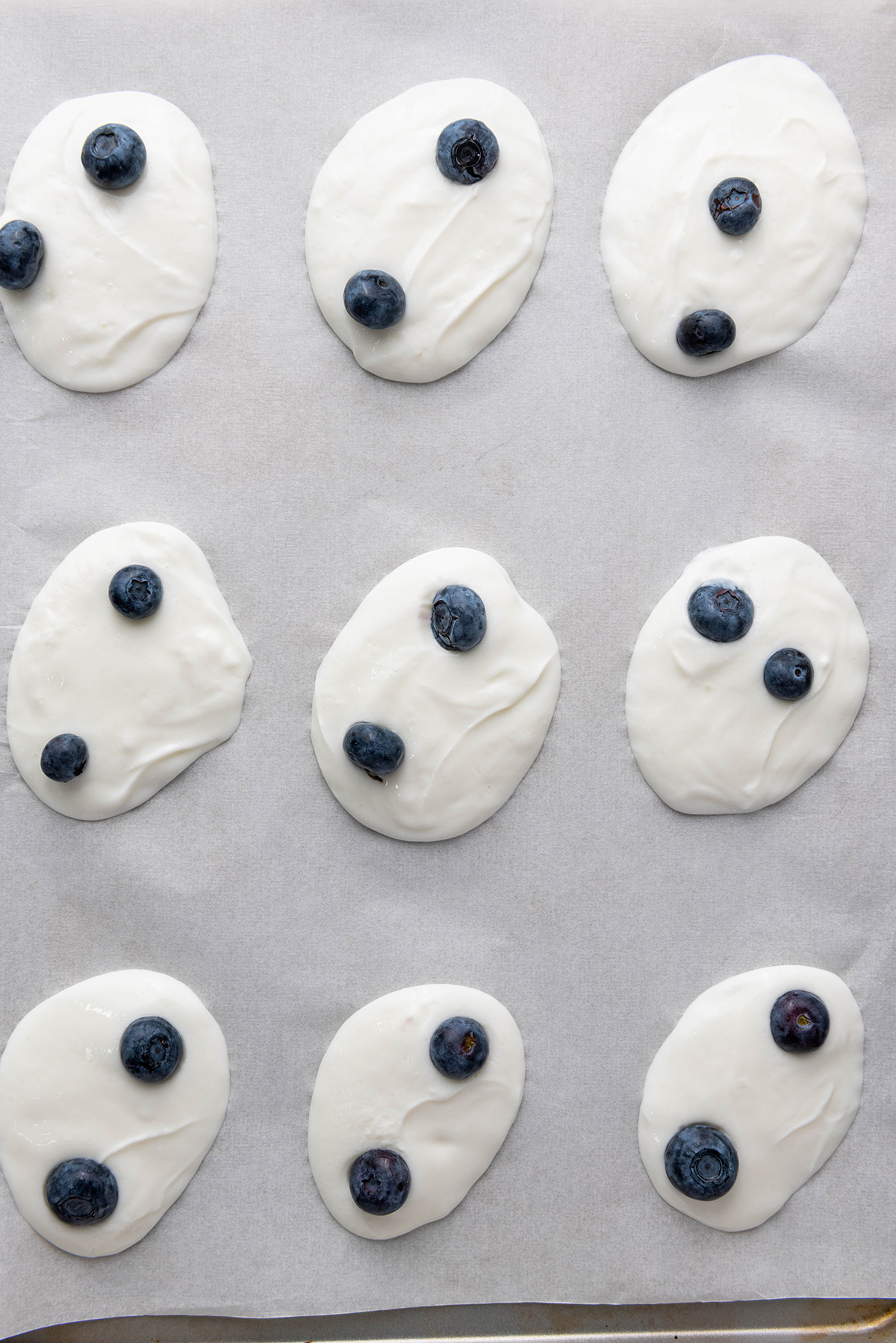Cool, creamy, and topped with fresh fruit and crunchy granola, this frozen Greek yogurt bark is an easy, healthy treat you can make in minutes. Greek yogurt dollops topped with blueberries only, arranged on parchment paper.