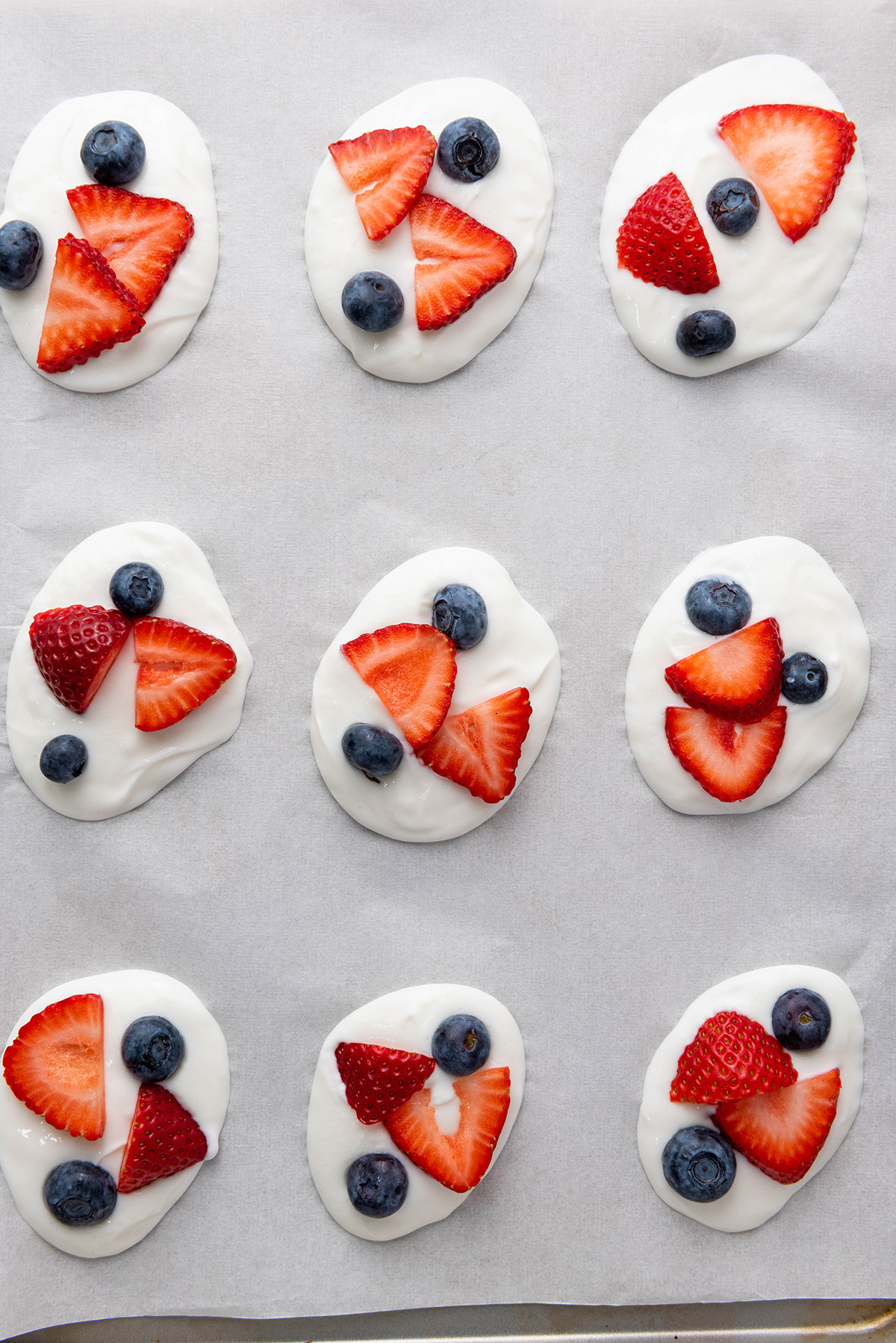 Cool, creamy, and topped with fresh fruit and crunchy granola, this frozen Greek yogurt bark is an easy, healthy treat you can make in minutes. Greek yogurt bark on parchment topped with strawberries and blueberries before sprinkling on granola.