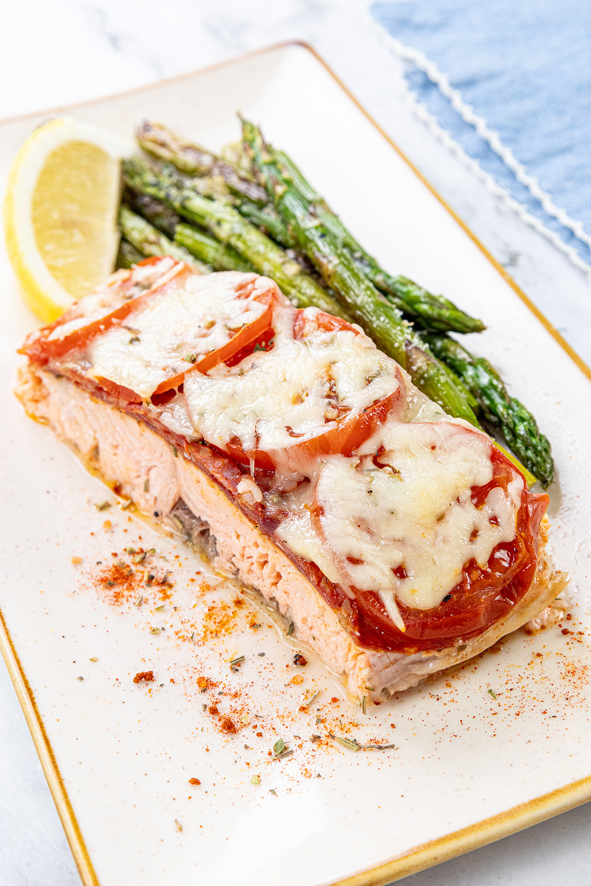Chilean style salmon topped with chorizo and cheese served on a plate with lemon and asparagus.