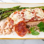 Chilean style salmon topped with chorizo and cheese served on a plate with lemon and asparagus.