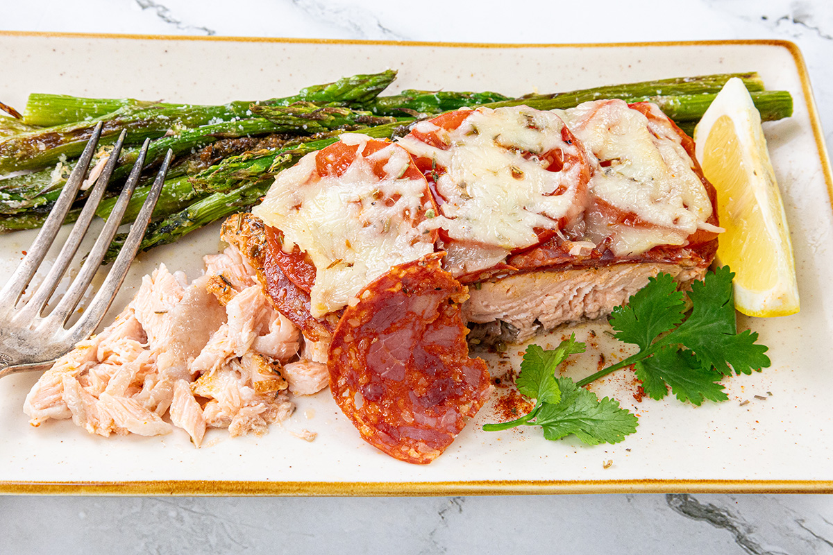 Chilean style salmon topped with chorizo and cheese served on a plate with lemon and asparagus.