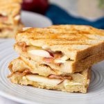 Stacked apple bacon and brie panini halves showing layers of brie, bacon, and apple slices.