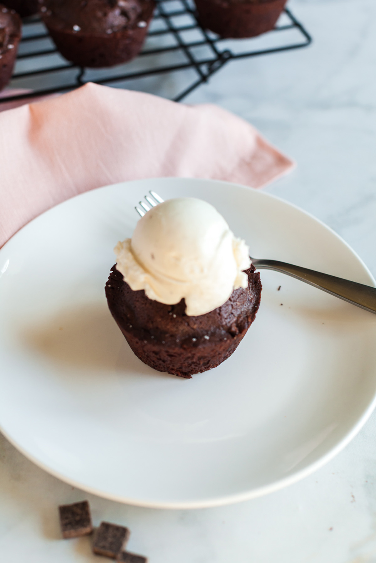 Part brownie, part cake, these brownie cakes are rich like a fudgy brownie but baked in cupcake form and made completely from scratch. Close-up overhead shot of a rich brownie cake topped with vanilla ice cream on a white plate with a fork.