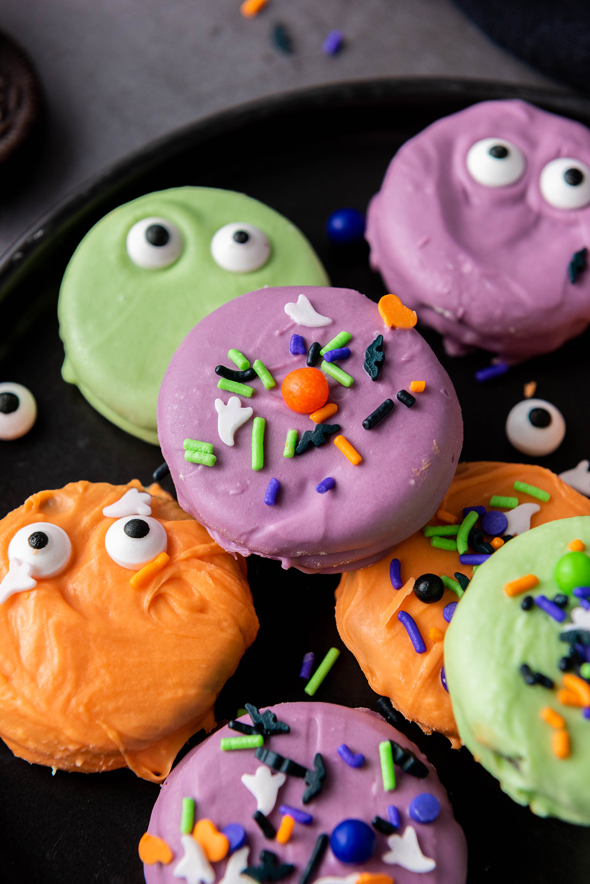Chocolate dipped Halloween Oreos on a serving plate with candy eyes and sprinkles.