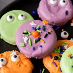 Assortment of decorated chocolate covered Halloween Oreos with different sprinkle patterns and candy eyes.