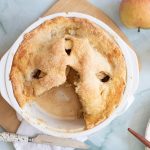Partially eaten double crust Honeycrisp apple pie in a white pie dish, showing baked apple filling inside.