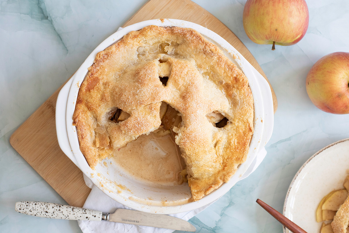 Partially eaten double crust Honeycrisp apple pie in a white pie dish, showing baked apple filling inside.