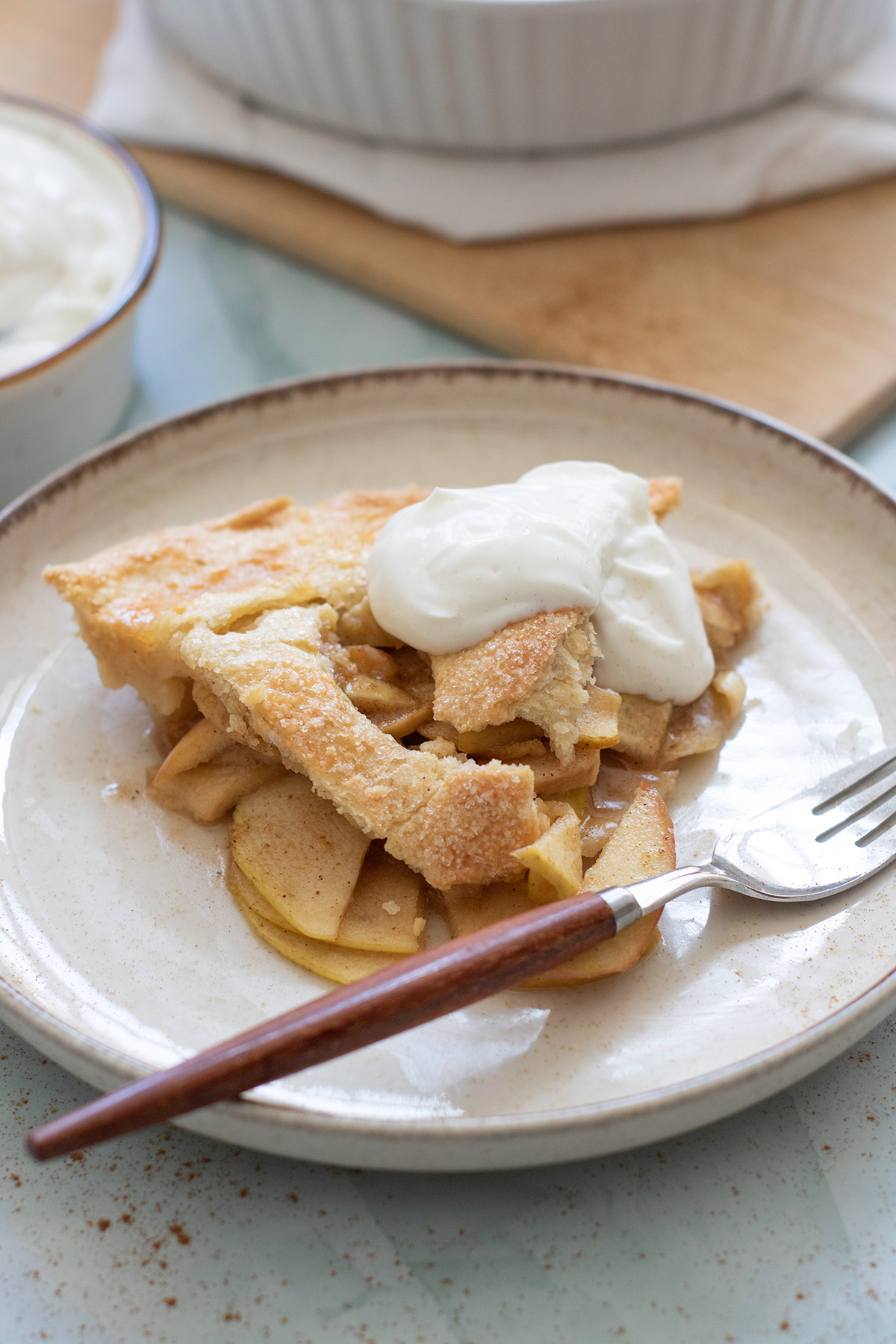 Slice of double crust Honeycrisp apple pie served on a plate with whipped cream topping.