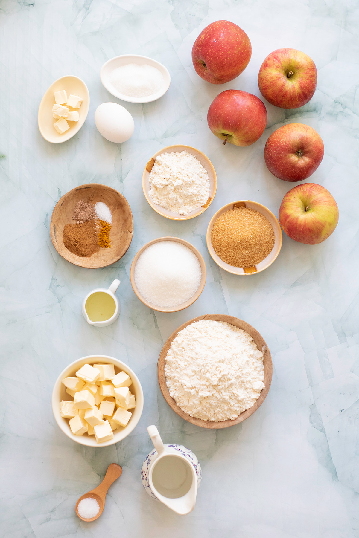 Honeycrisp apple pie ingredients laid out, including fresh apples, flour, butter, sugars, spices, and egg.