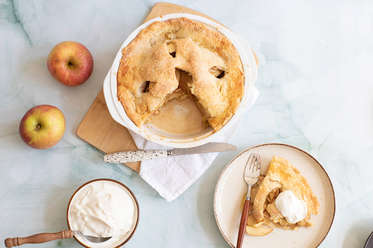 A double crust honeycrisp apple pie with one slice on a plate.
