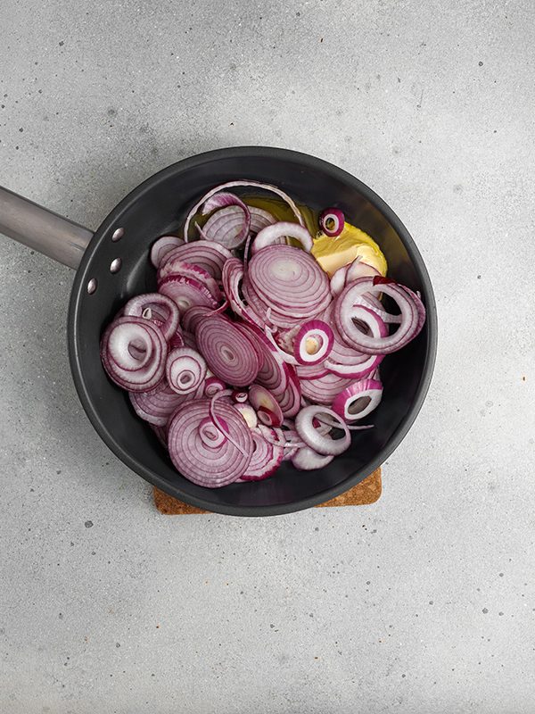 Flaky pastry, sweet caramelized onions and a creamy egg and Gruyere cheese filling make this onion tart both flavorful and irresistible to serve as an appetizer, dinner or even brunch. Sliced red onions and butter in a skillet, ready to be sautéed for caramelized onion filling.