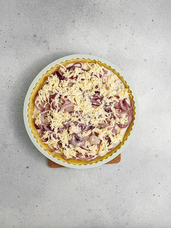 Flaky pastry, sweet caramelized onions and a creamy egg and Gruyere cheese filling make this onion tart both flavorful and irresistible to serve as an appetizer, dinner or even brunch. Tart crust filled with caramelized onions and topped with grated cheese, ready to go into the oven.