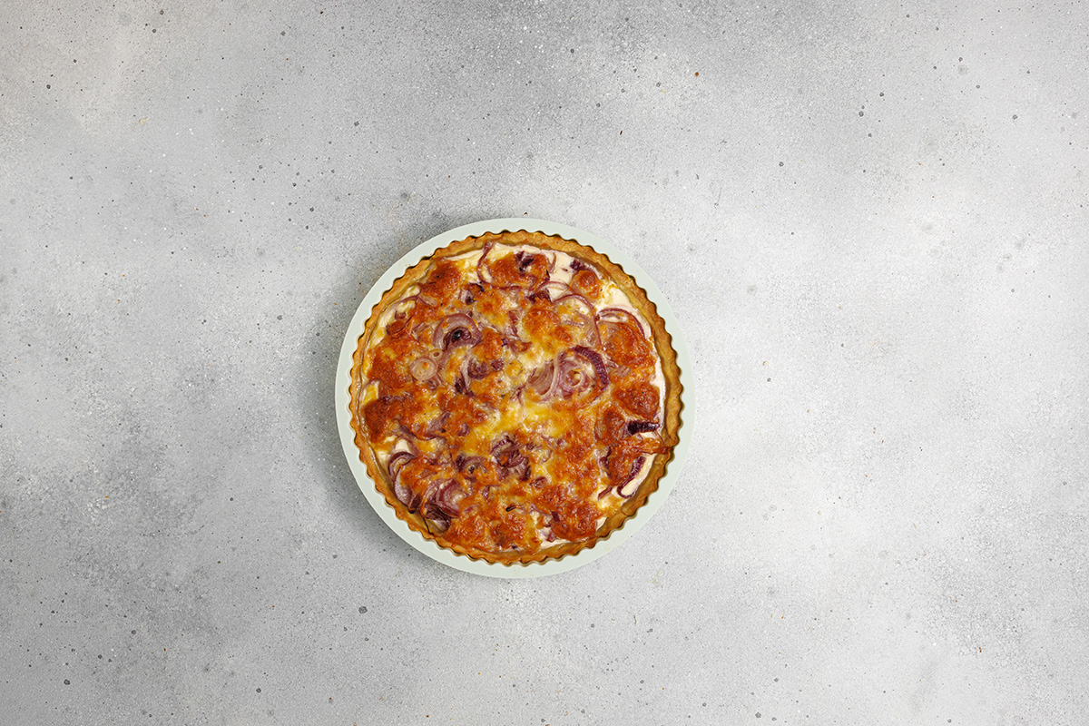 Flaky pastry, sweet caramelized onions and a creamy egg and Gruyere cheese filling make this onion tart both flavorful and irresistible to serve as an appetizer, dinner or even brunch. A golden-brown caramelized onion tart in a fluted tart pan, fresh from the oven on a gray surface.