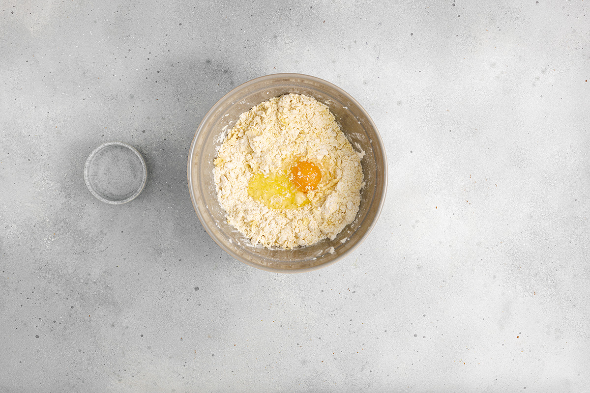 Flaky pastry, sweet caramelized onions and a creamy egg and Gruyere cheese filling make this onion tart both flavorful and irresistible to serve as an appetizer, dinner or even brunch. Flour and butter mixture in a bowl with an egg cracked in the center, ready to be combined into dough.