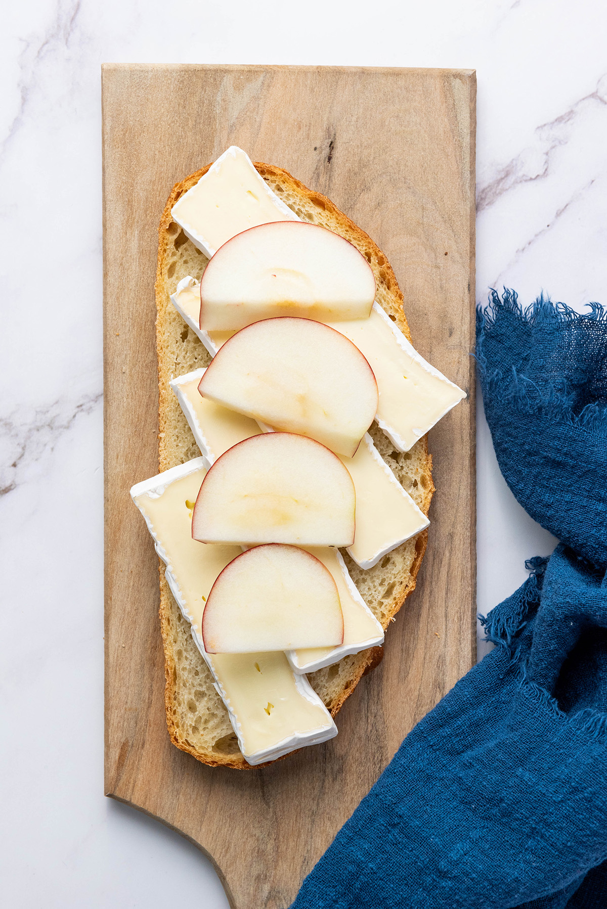 Sourdough bread topped with brie cheese slices and fresh apple slices, the first step in making an apple bacon and brie panini.