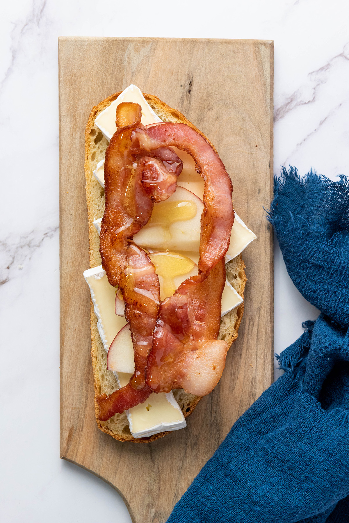Crispy bacon layered over brie and apple slices with a drizzle of honey on bread for apple bacon and brie panini."