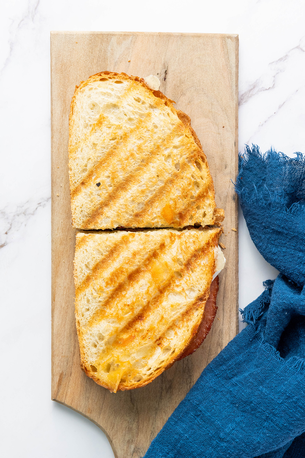 Golden grilled apple bacon and brie panini cut in half on a wooden board.