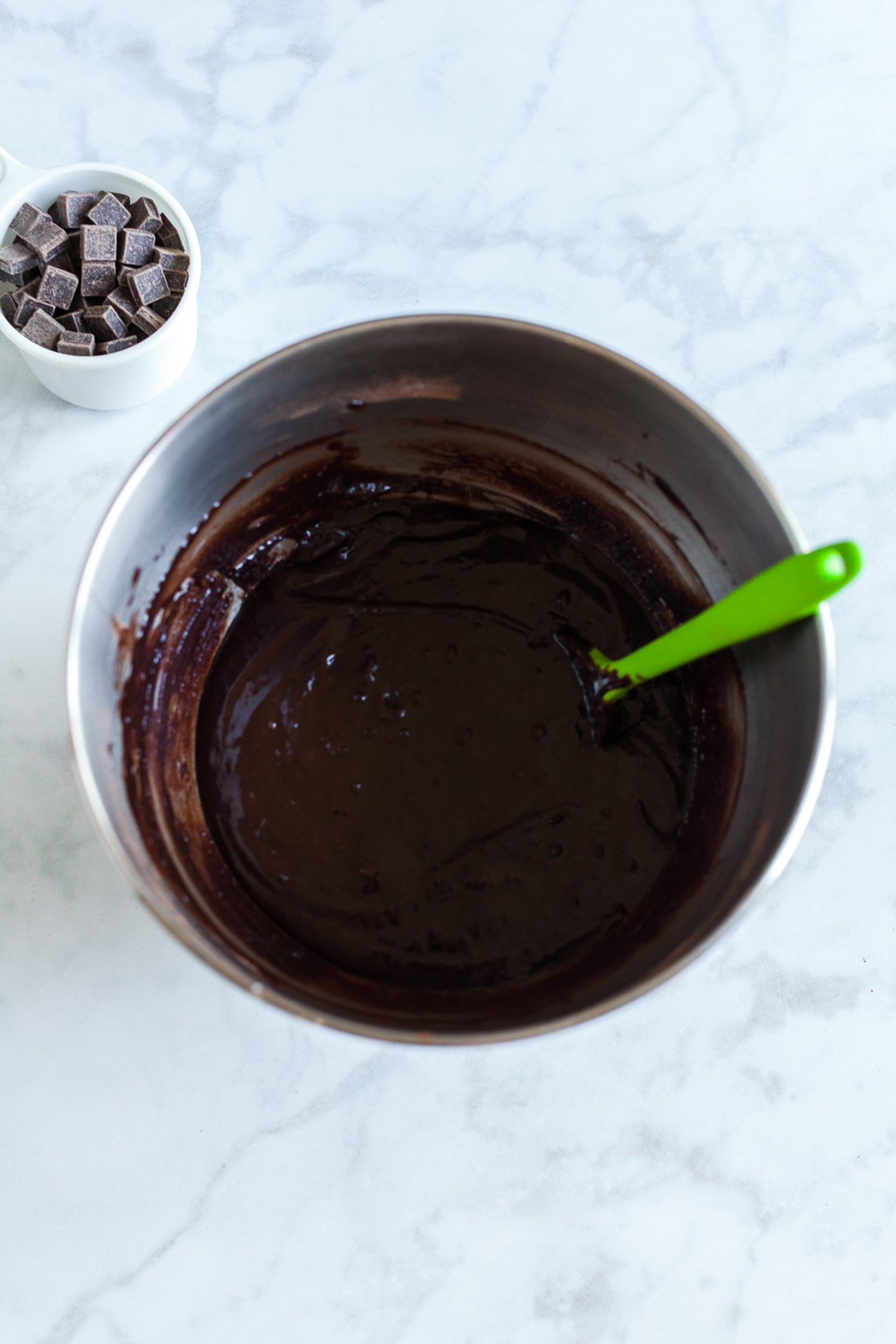 Part brownie, part cake, these brownie cakes are rich like a fudgy brownie but baked in cupcake form and made completely from scratch. Thick, glossy chocolate brownie batter in a mixing bowl with a green spatula.