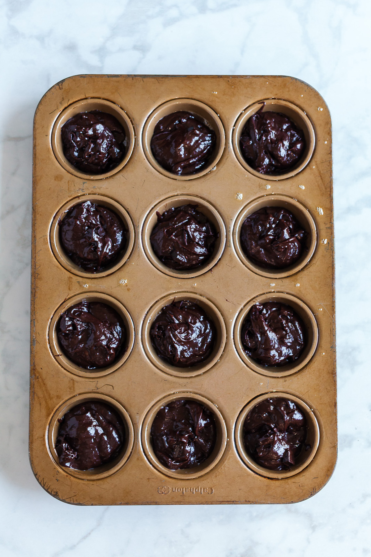 Part brownie, part cake, these brownie cakes are rich like a fudgy brownie but baked in cupcake form and made completely from scratch. Brownie cupcake batter scooped into a greased 12-cup muffin tin, ready to bake.