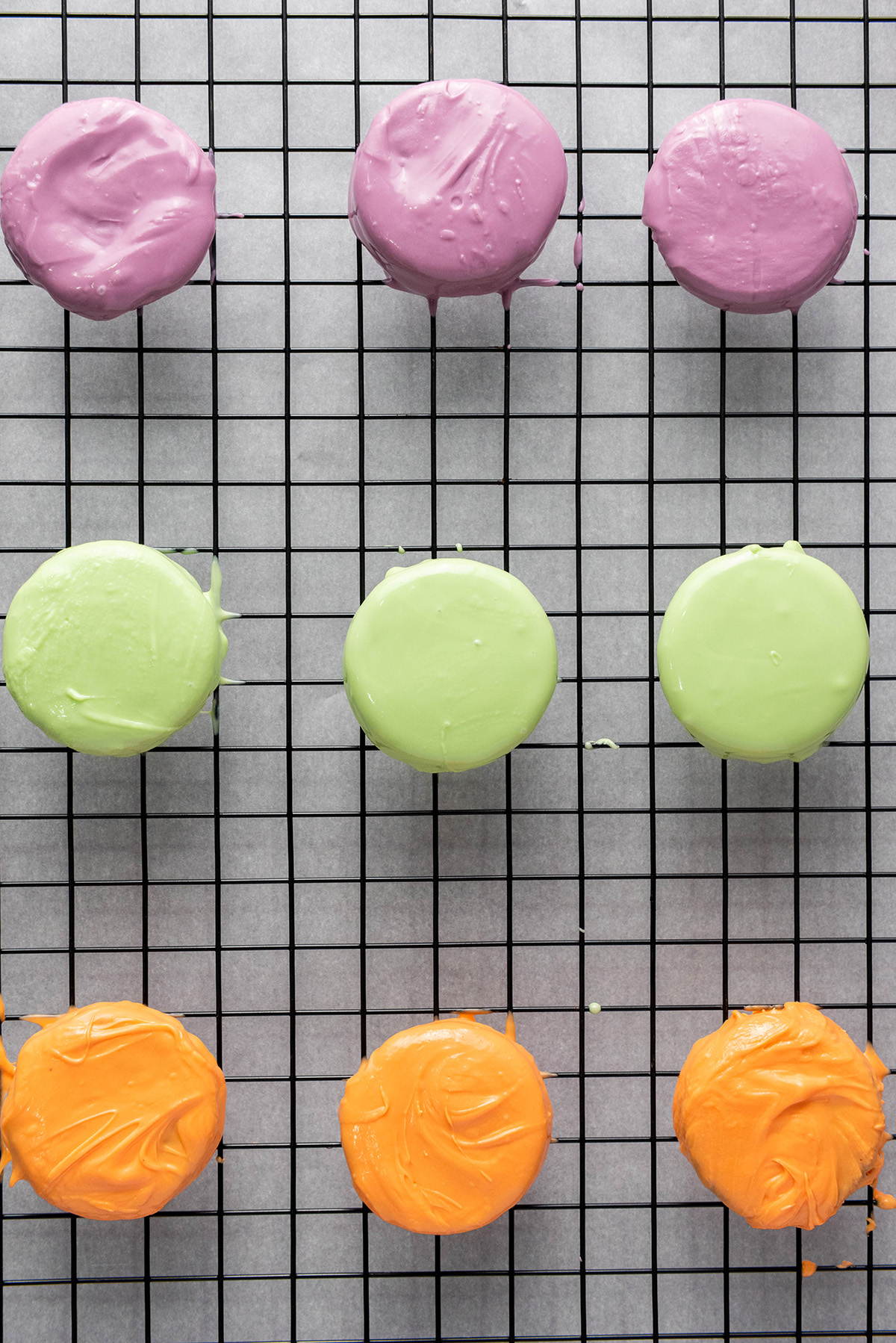 These chocolate covered Halloween Oreos are the easiest spooky treat! Dip, decorate, and serve a colorful no-bake treat that’s just as fun to decorate as it is to eat! Freshly dipped Oreos in green, purple, and orange candy melts cooling on a wire rack.