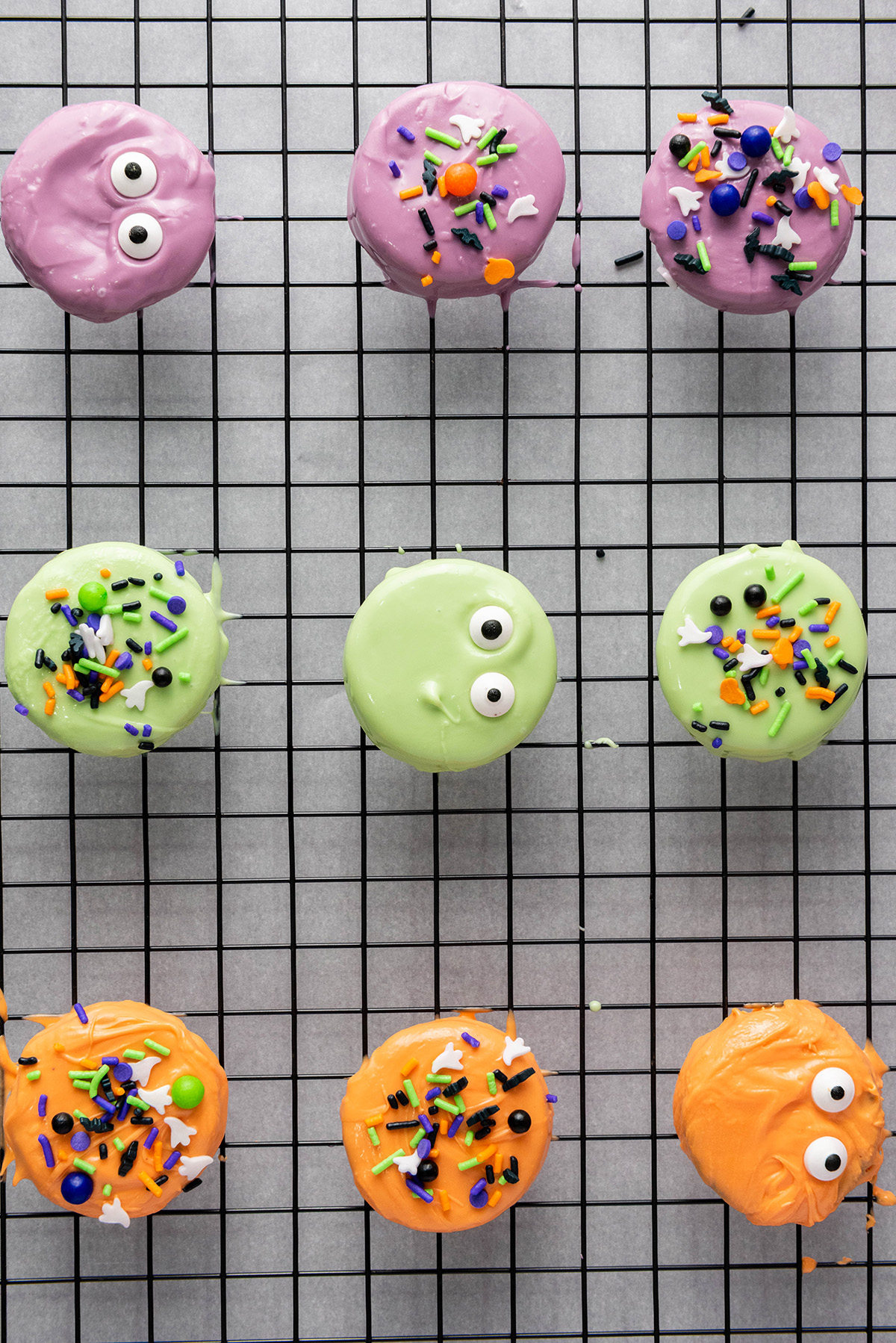 These chocolate covered Halloween Oreos are the easiest spooky treat! Dip, decorate, and serve a colorful no-bake treat that’s just as fun to decorate as it is to eat! Overhead shot of colorful chocolate covered Halloween Oreos on a cooling rack, topped with candy eyes and sprinkles.