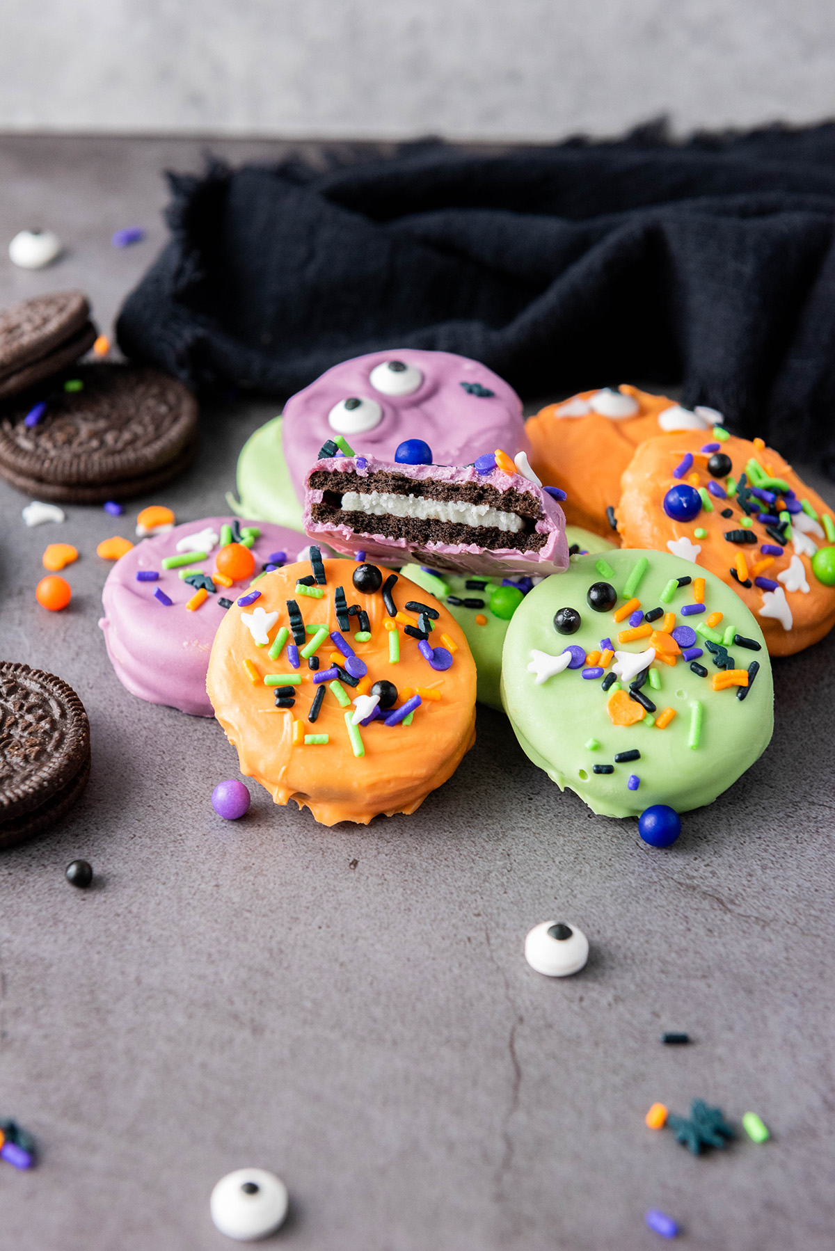 These chocolate covered Halloween Oreos are the easiest spooky treat! Dip, decorate, and serve a colorful no-bake treat that’s just as fun to decorate as it is to eat! Close-up of a chocolate dipped Halloween Oreo with a bite taken out, showing the cream filling inside.