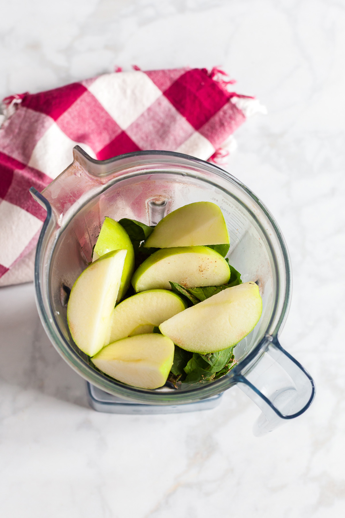 Overhead view of fresh spinach leaves and green apple wedges in a blender, ready to make a spinach green apple smoothie.