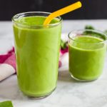 Horizontal view of spinach apple smoothies in two glasses, garnished with a yellow straw in one.