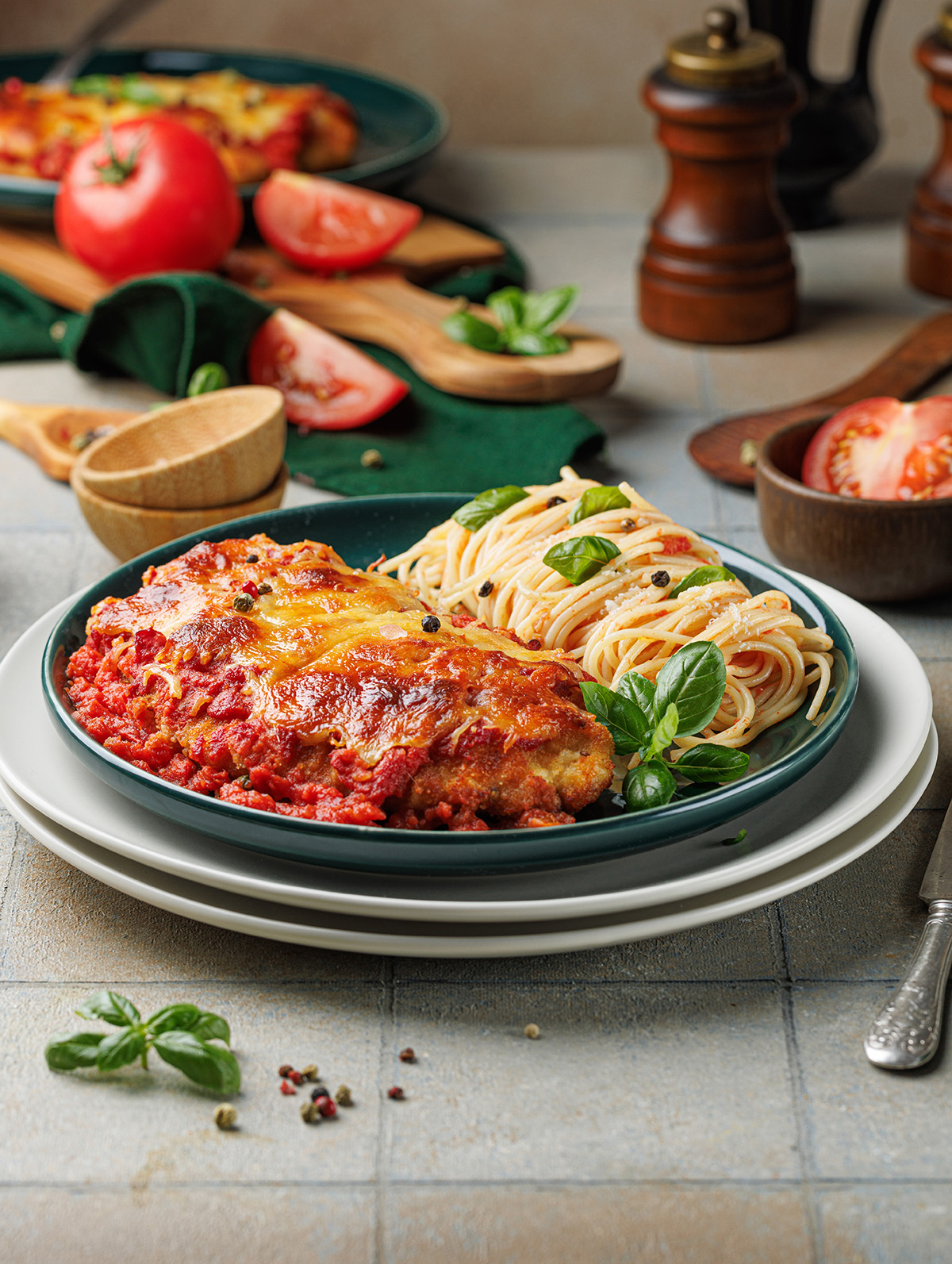 Crispy baked chicken Parmesan with spaghetti marinara, topped with basil and Parmesan cheese on a green plate.