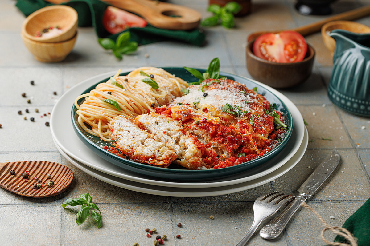 Chicken parmesan with marinara plated with spaghetti.