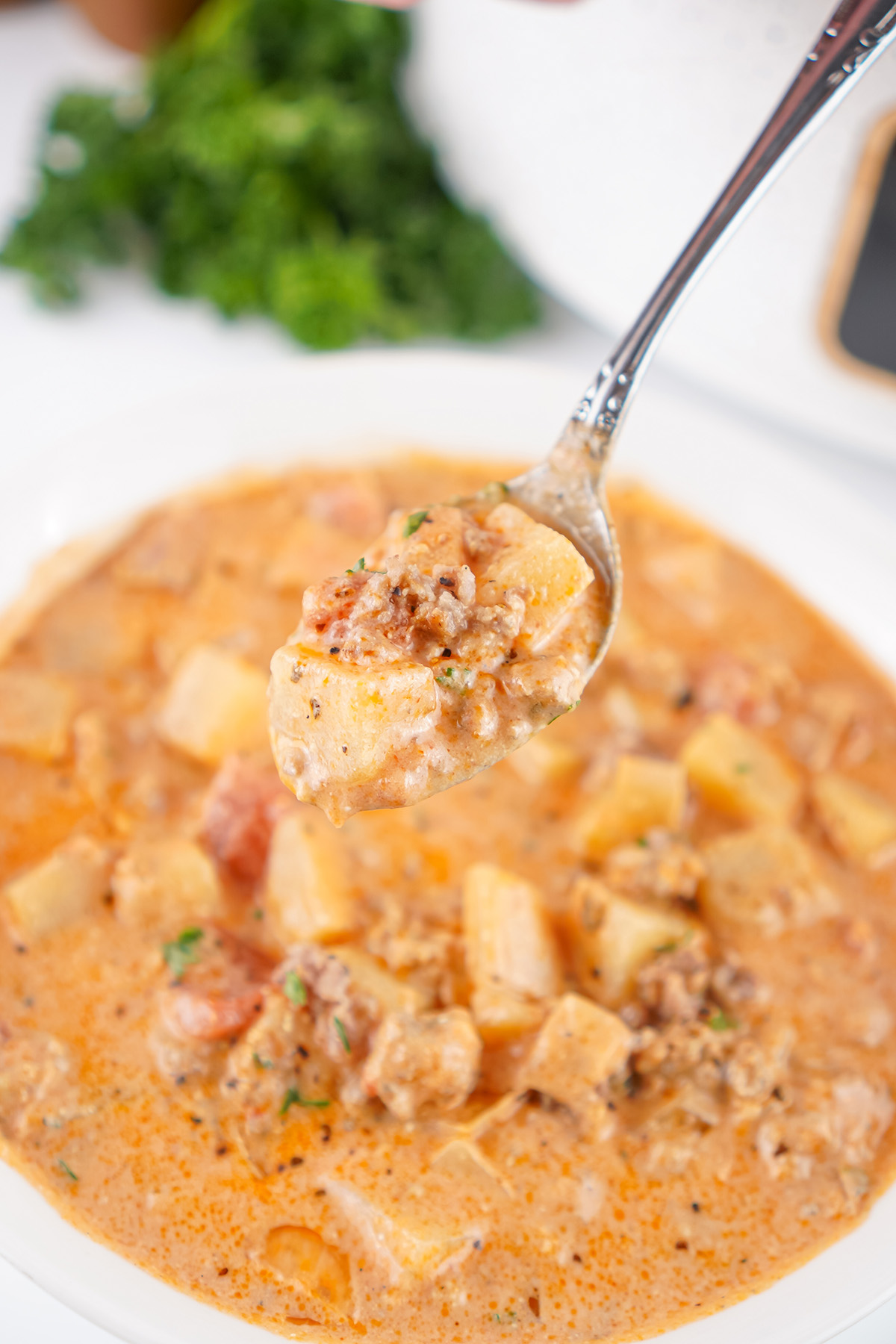 Close-up of a spoonful of creamy slow cooker sausage potato soup with chunks of potatoes, sausage, and tomatoes.