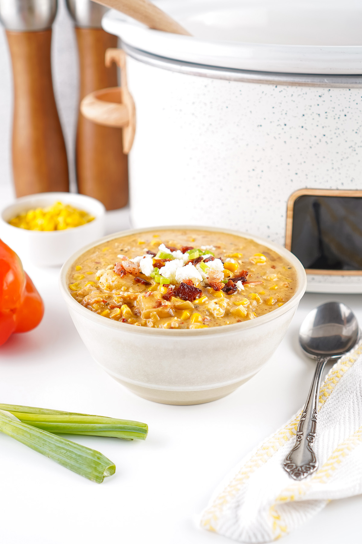 Overhead view of creamy slow cooker Mexican street corn soup being stirred with a wooden spoon, garnished with bacon, queso fresco, and green onions.