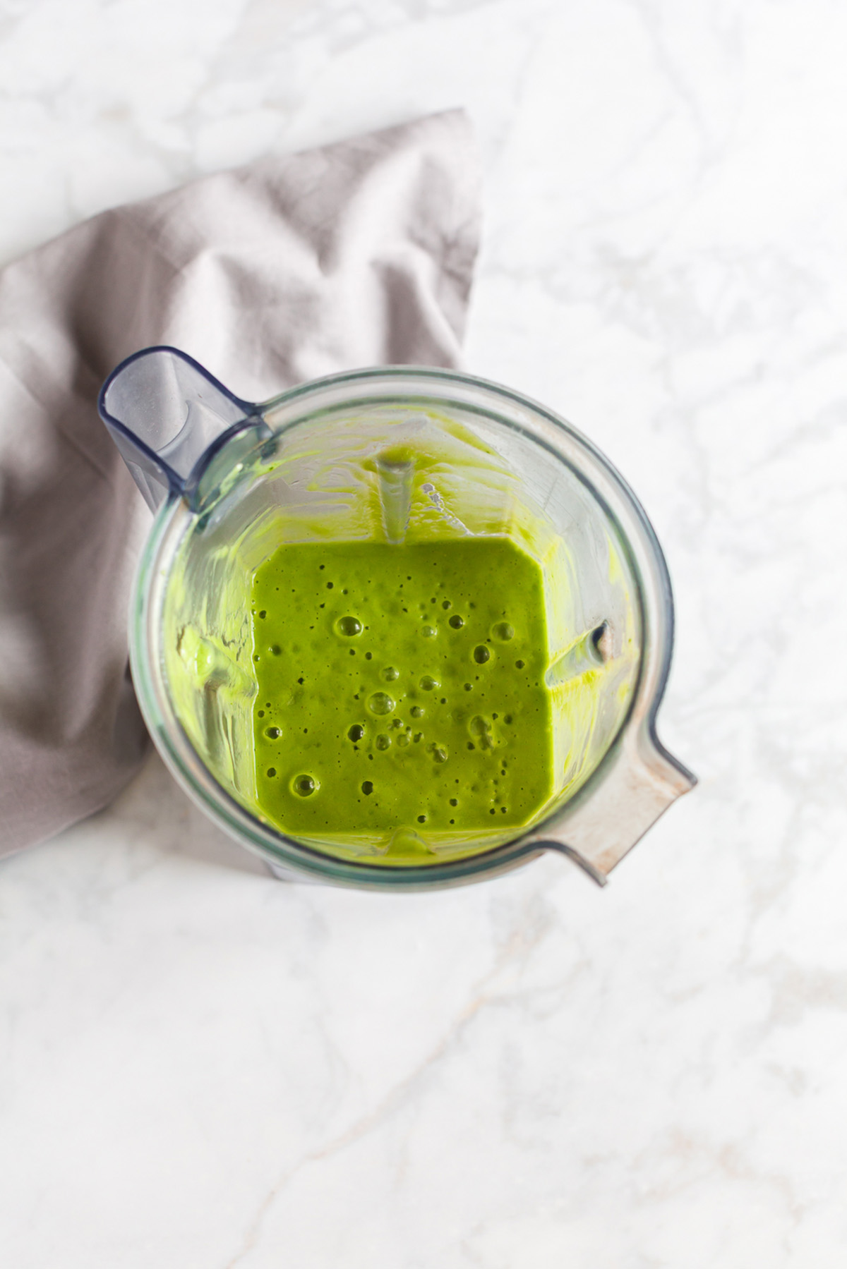 Overhead view of blender filled with blended pear spinach smoothie on marble surface.
