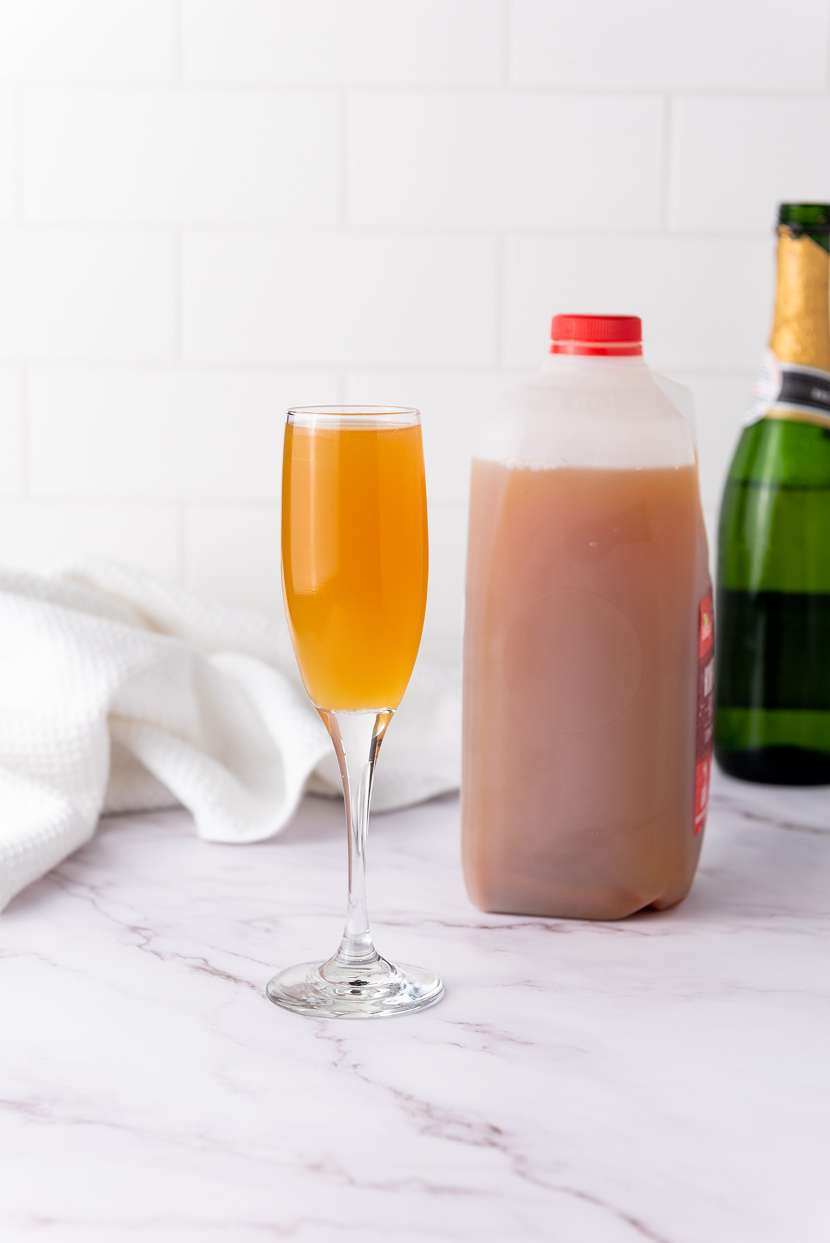 A green champagne bottle and a half-gallon jug of apple cider side by side on a marble countertop.