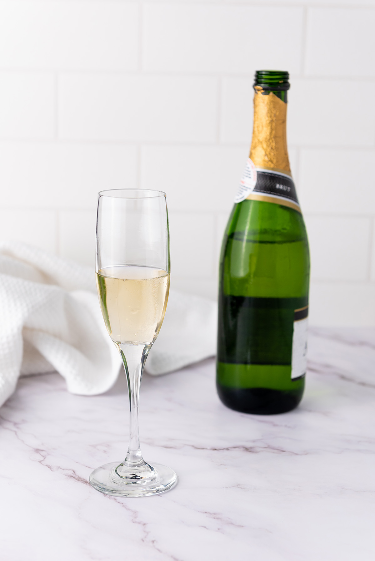 A glass of chilled champagne next to an open bottle, ready to be mixed with apple cider for a mimosa.