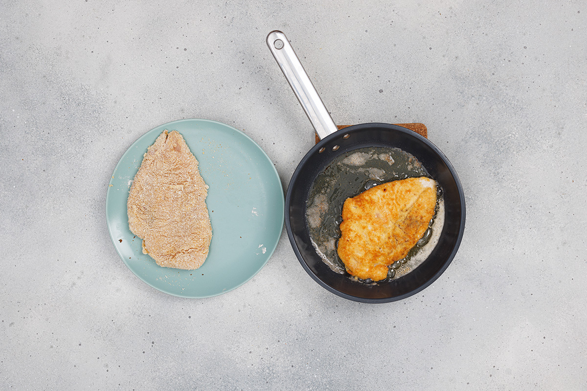Chicken breast being pan-fried until golden brown in a skillet for homemade chicken Parmesan.