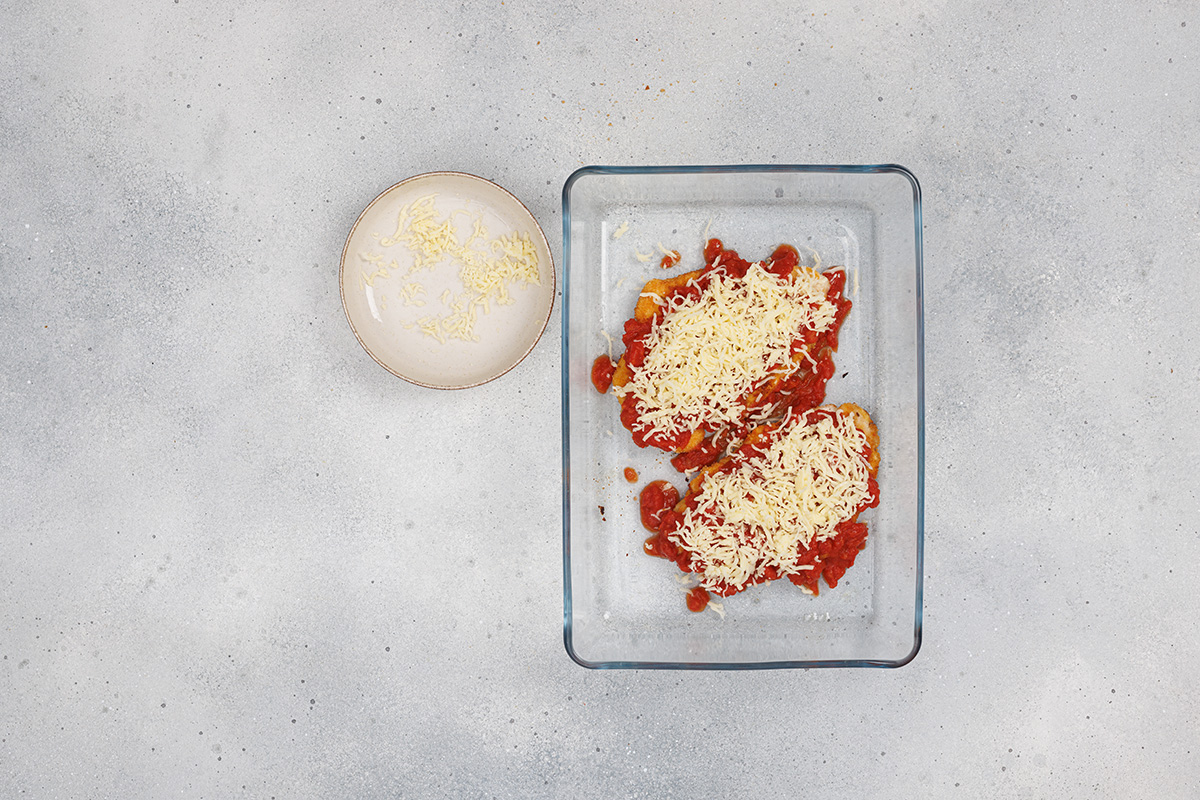 Chicken breasts topped with marinara sauce and mozzarella cheese in a baking dish, ready to bake for classic chicken Parmesan.