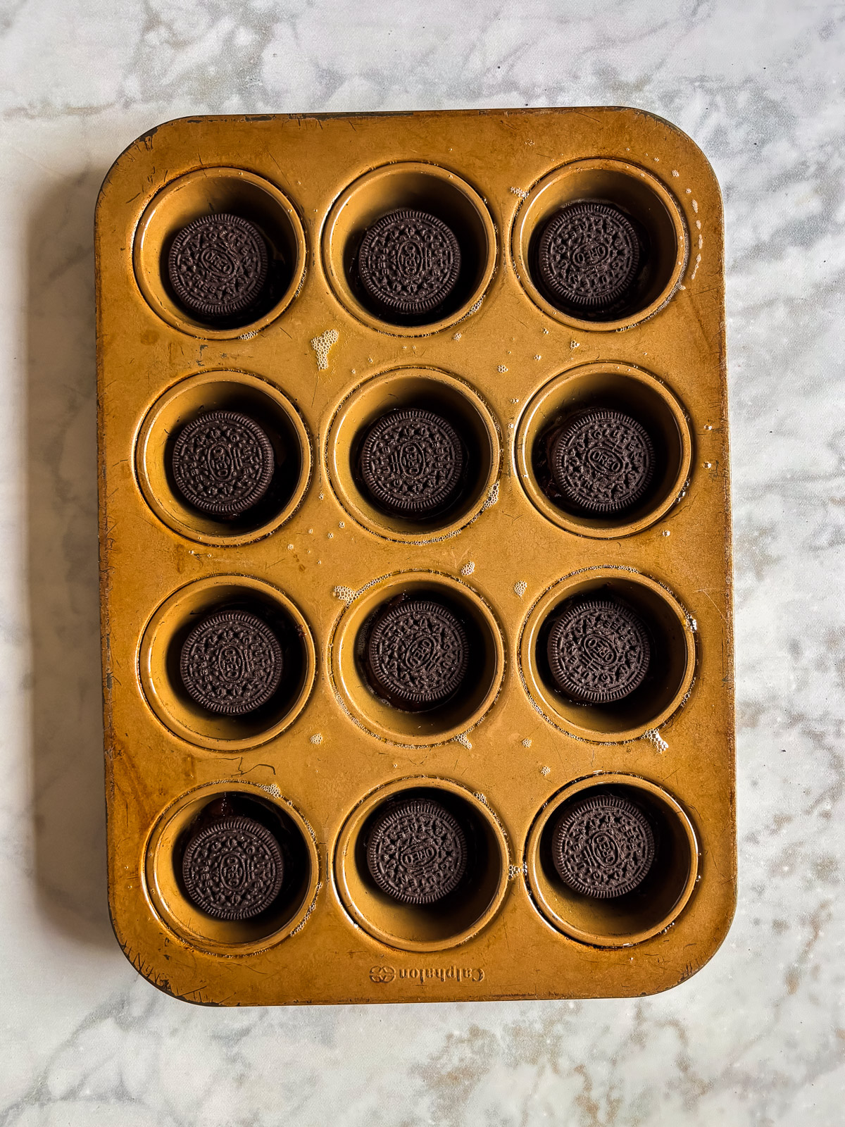 Cupcake pan filled with Oreos placed in the bottom of each muffin cup.