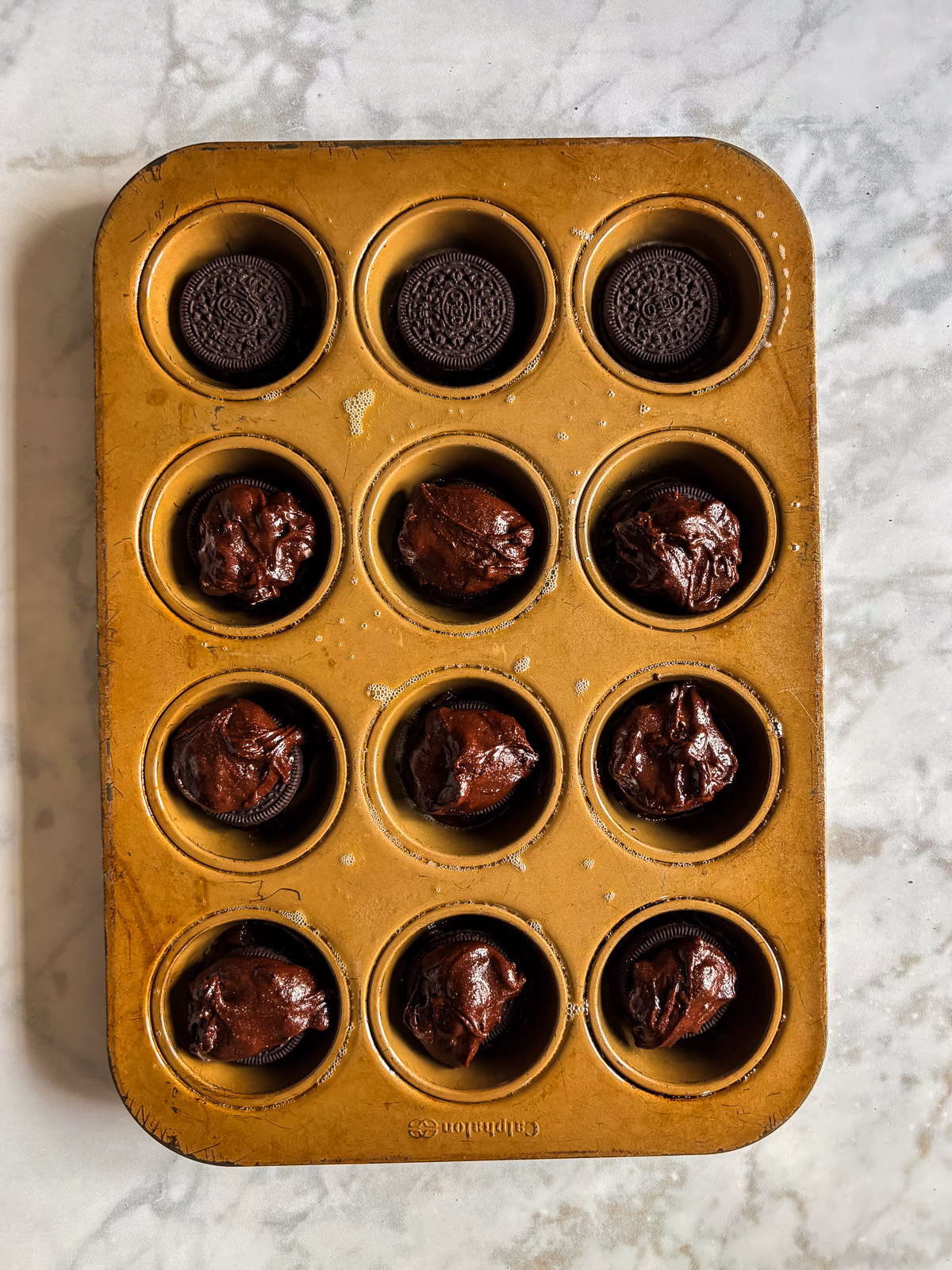 Brownie batter scooped on top of Oreos in a muffin tin.