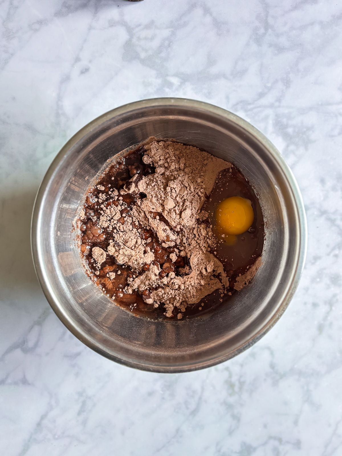 Mixing brownie batter with an egg and dry mix in a stainless steel bowl.