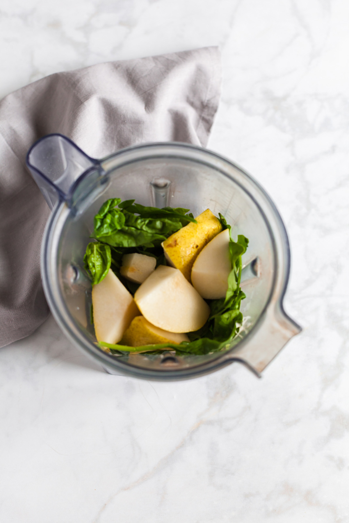Blender filled with fresh spinach, pear chunks, and banana pieces before blending pear smoothie.