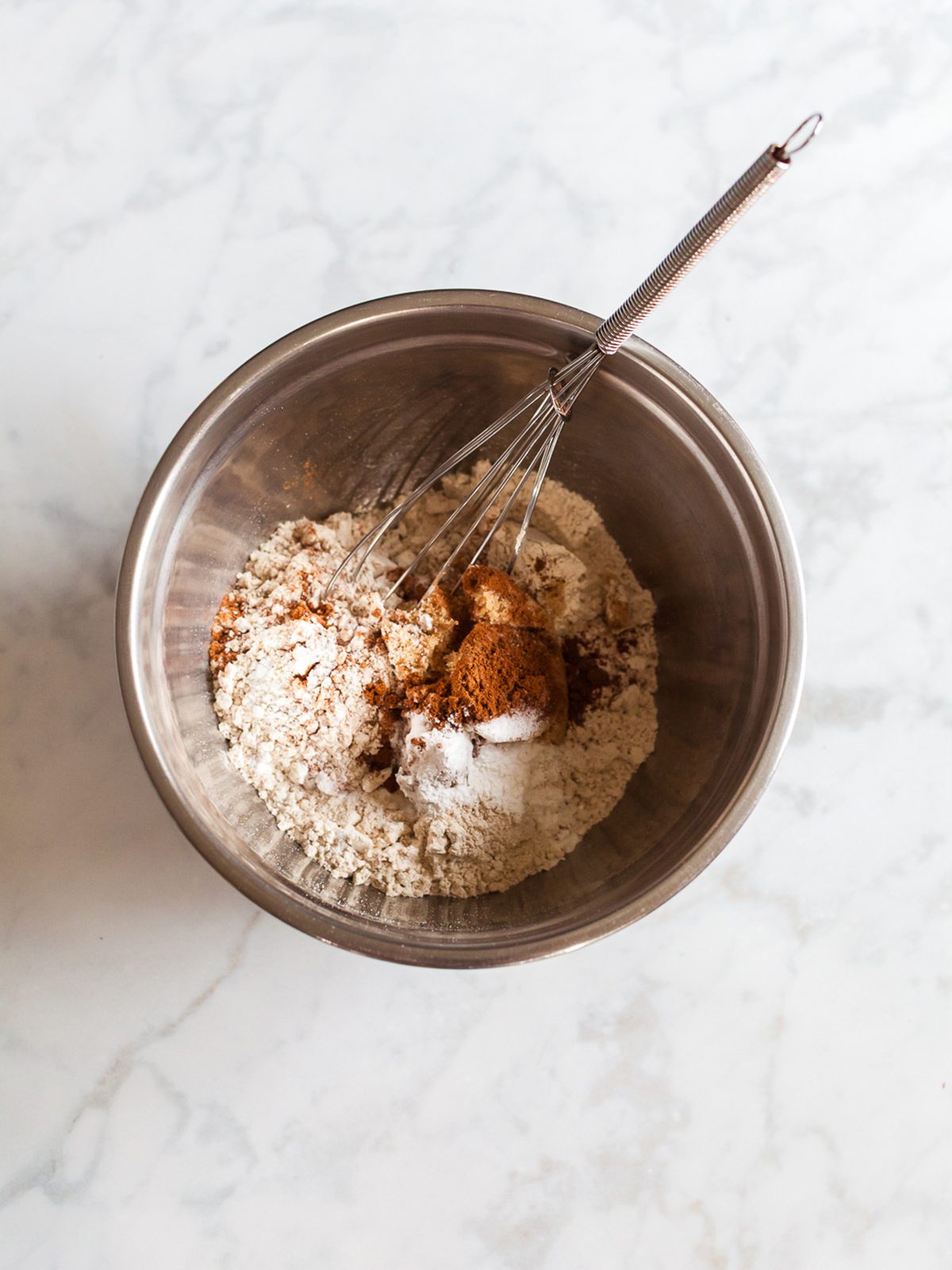 Whisking oat flour, cinnamon, pumpkin pie spice, and leavening in a metal bowl to make pumpkin oat breakfast cookies.